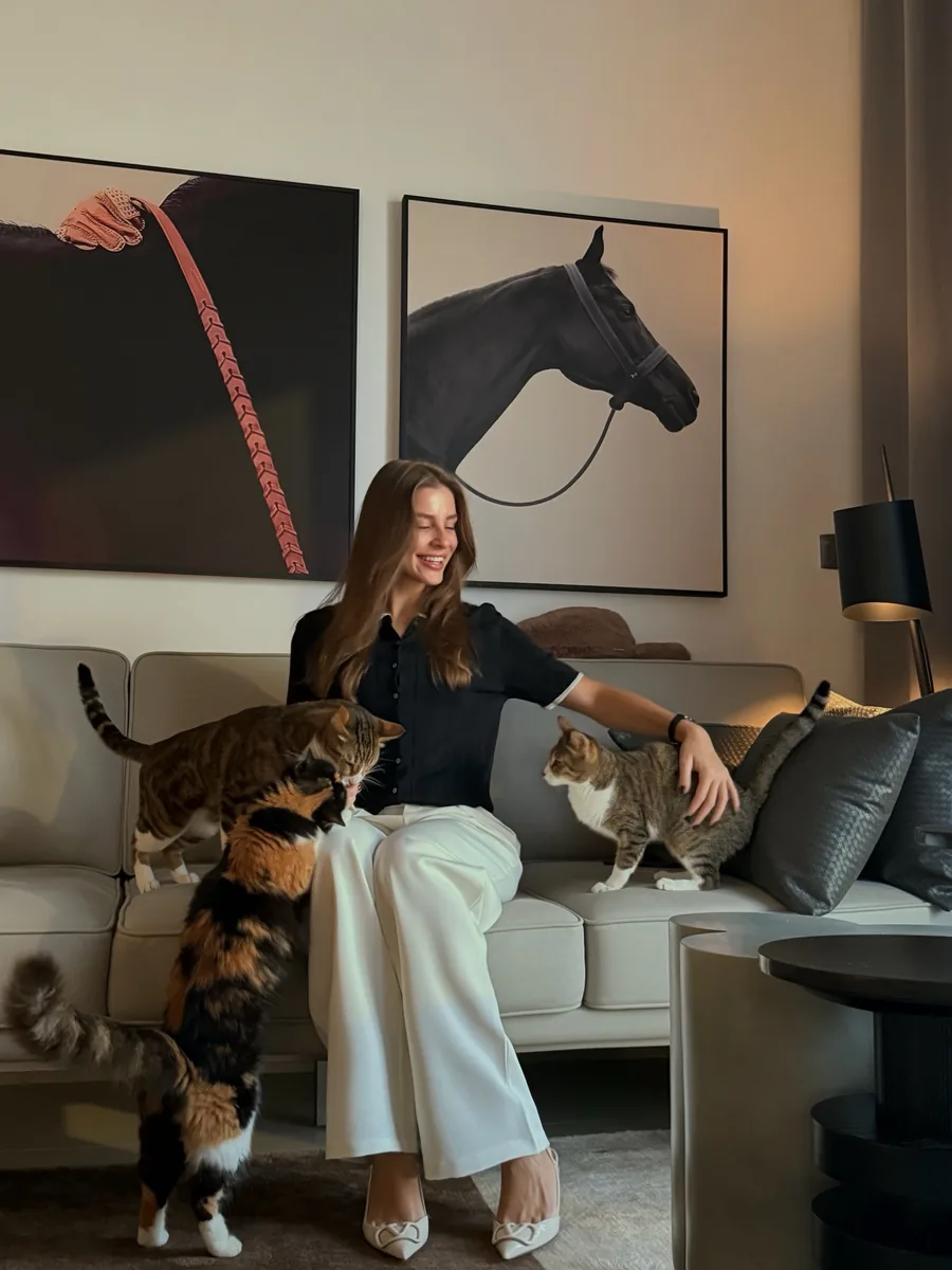 Tania, the founder of Furry Affairs, smiling on the sofa at home with three cats